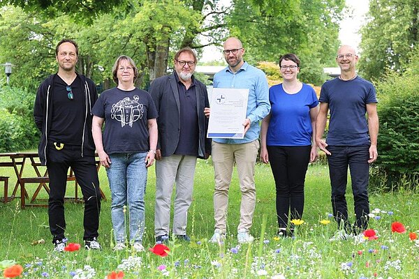 Zwei Frauen und vier Männer stehen im Grünen und schauen in die Kamera.