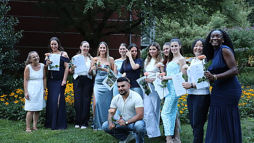 Eine Gruppe junger Menschen steht im Grünen, alle halten Urkunden und Blumen in den Händen. 