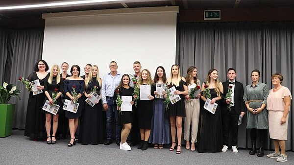 Feierlich gekleidete Menschen halten Urkunden in den Händen und freuen sich. 