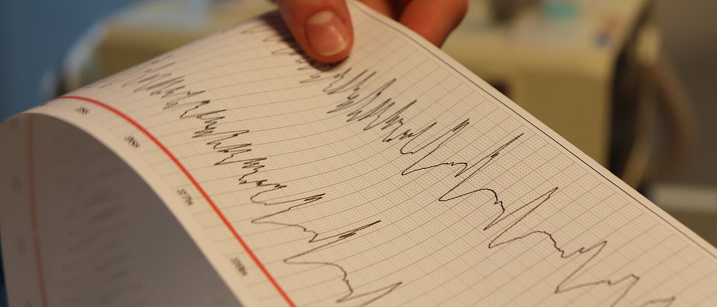 Eine Hand hält den Ausdruck einer EEG-Aufzeichnung. 