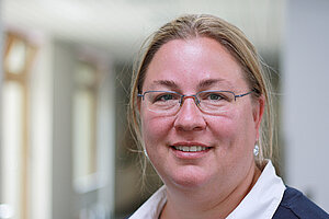 Portrait einer Frau mit blonden zusammengebundenen Haaren und einer dünnrandigen silbernen Brille.