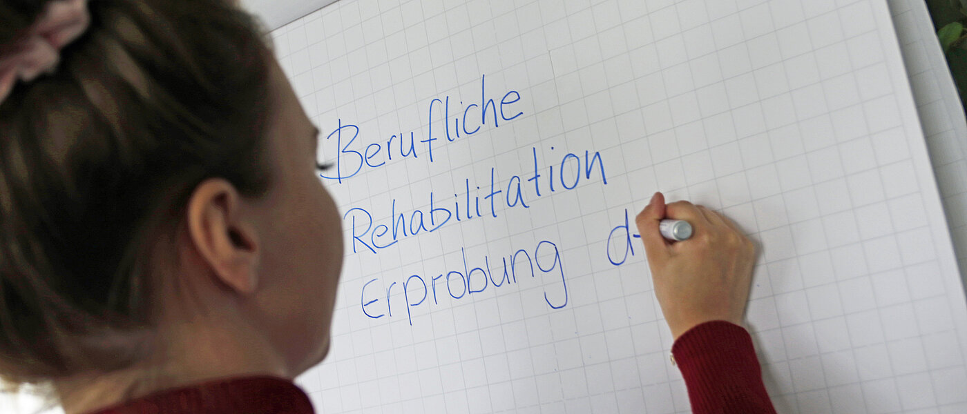 Eine Frau schreibt etwas auf ein Flipchart mit einem blauem Stift.