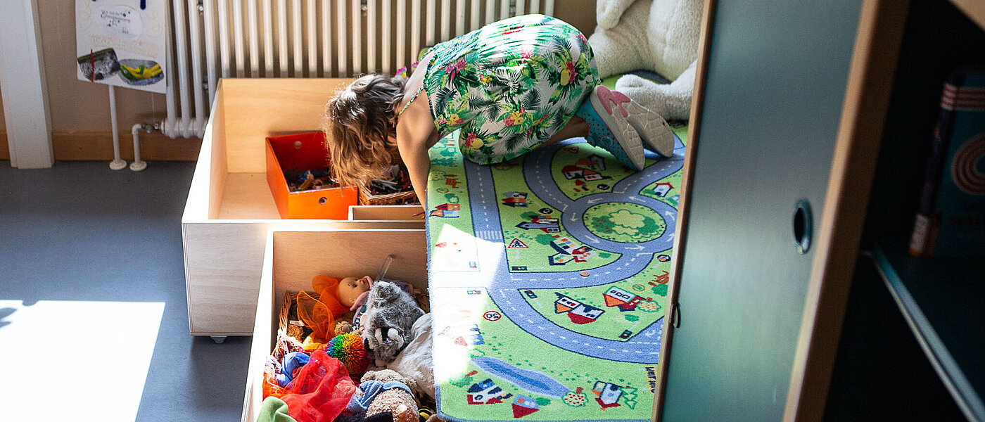 Mädchen im Kinderzimmer, sie sucht Spielsachen in einer Holzkiste