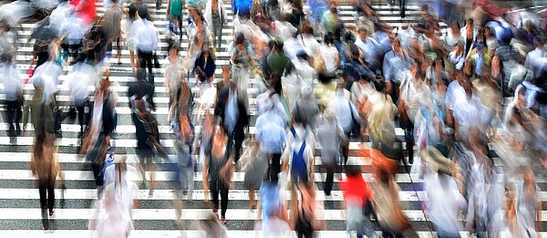 über einen sehr breiten Zebrastreifen laufen sehr viele Menschen. Sie sind nur unscharf abgebildet.
