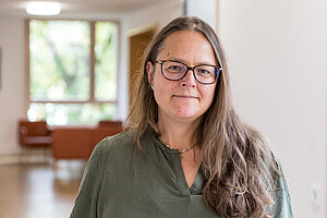 Eine Frau mit Brille, braunen Haaren und grünem Oberteil blickt freundlich in die Kamera.