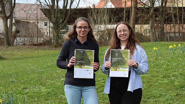Zwei junge Frauen, beide mit Brille, halten den Nachhaltigkeitsbericht in den Händen.