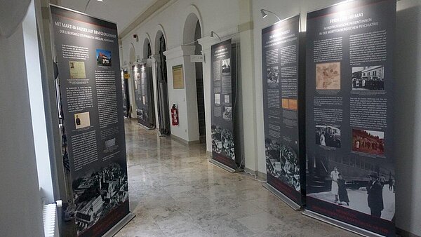 An den Wänden entlang eines dunklen Flurs stehen Roll-ups einer Wanderausstellung.