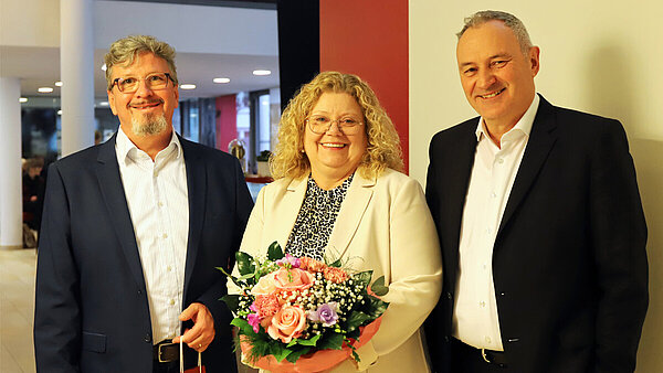 Drei Personen, zwei Männer und eine Frau, stehen nebeneinander und lächeln in Richtung Kamera.