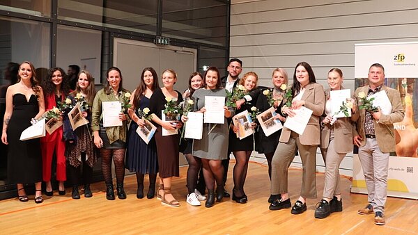 Eine fröhliche Gruppe festlich gekleideter junger Menschen, die eine Urkunde in den Händen halten. 