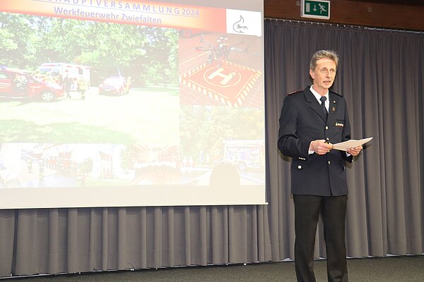 Ein Mann in Feuerwehruniform steht vor einer Leinwand. 