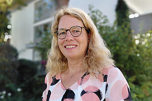 Eine Frau im mittleren Alter mit braunen Locken und einer Brille. 