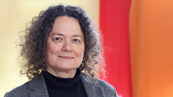 Brünette Frau lächelt in die Kamera, der Hintergrund ist in Rottönen gehalten.