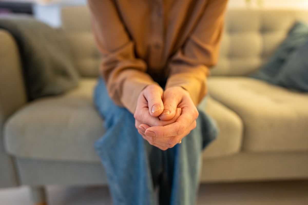 Nahaufnahme einer auf einem Sofa sitzenden Person, die die Hände in den Schoß gelegt hat.